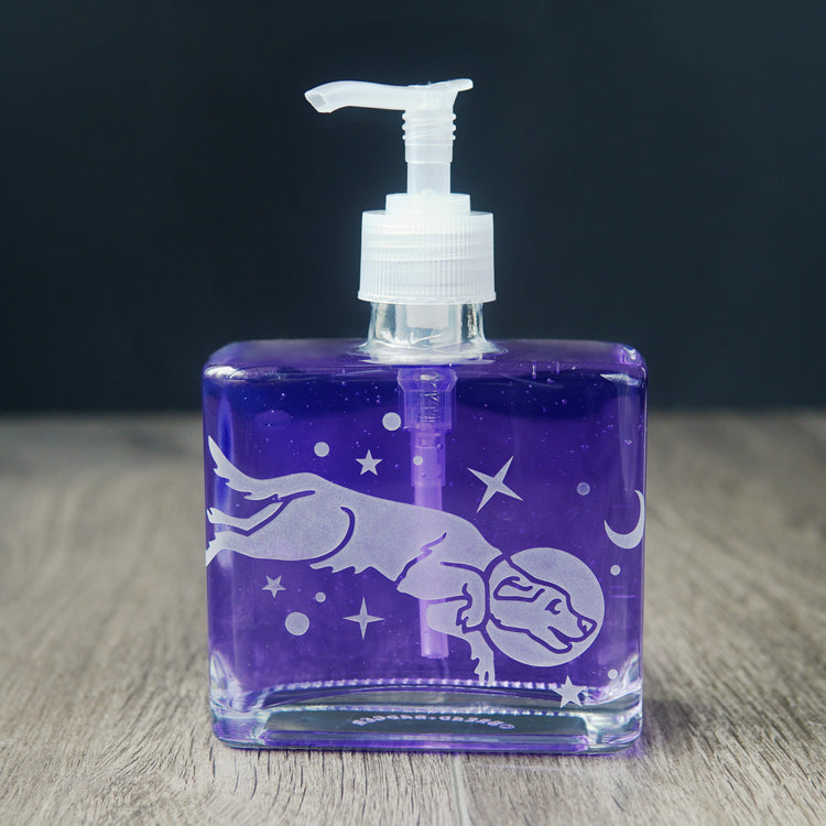 a square glass space dog soap dispenser filled with purple dish soap