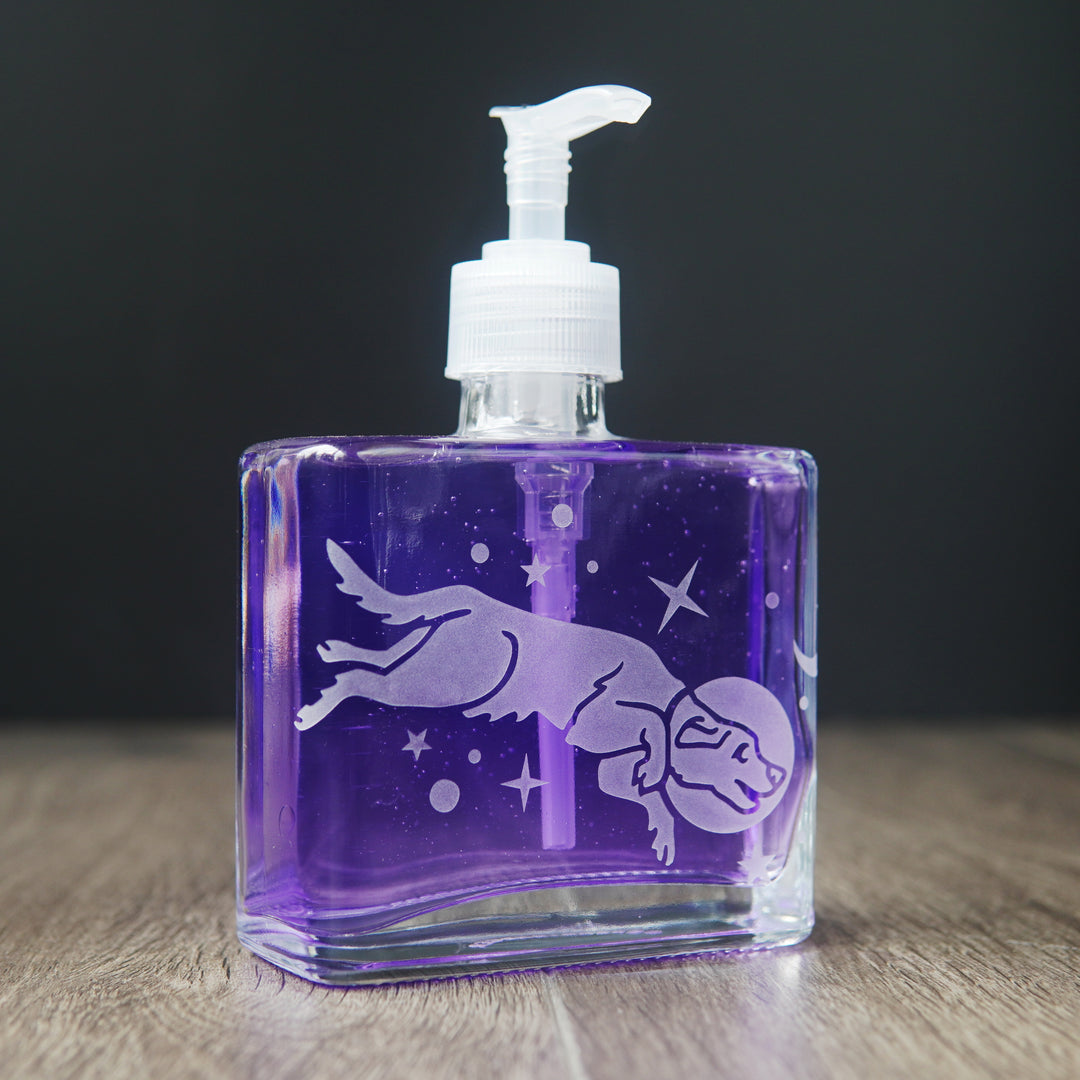 a square glass space dog soap dispenser filled with purple dish soap