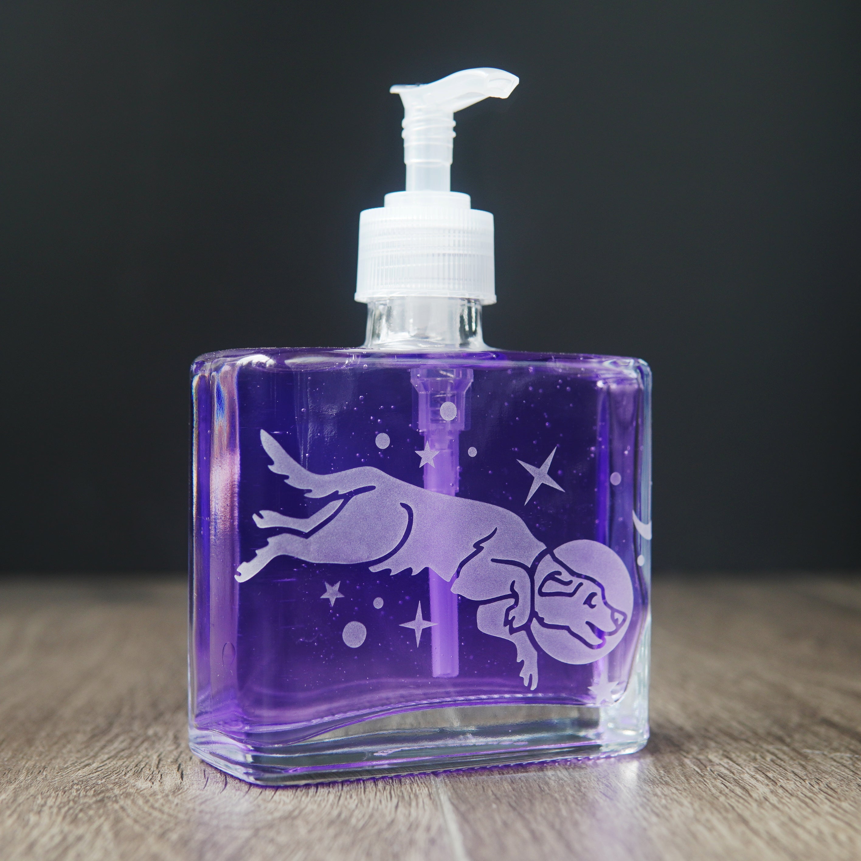 a square glass space dog soap dispenser filled with purple dish soap