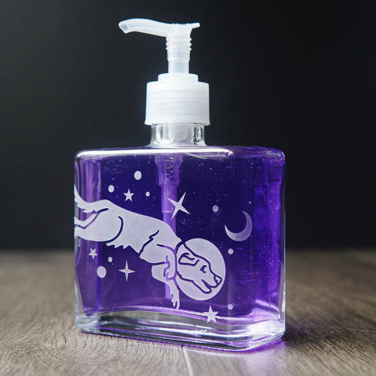 a square glass space dog soap dispenser filled with purple dish soap