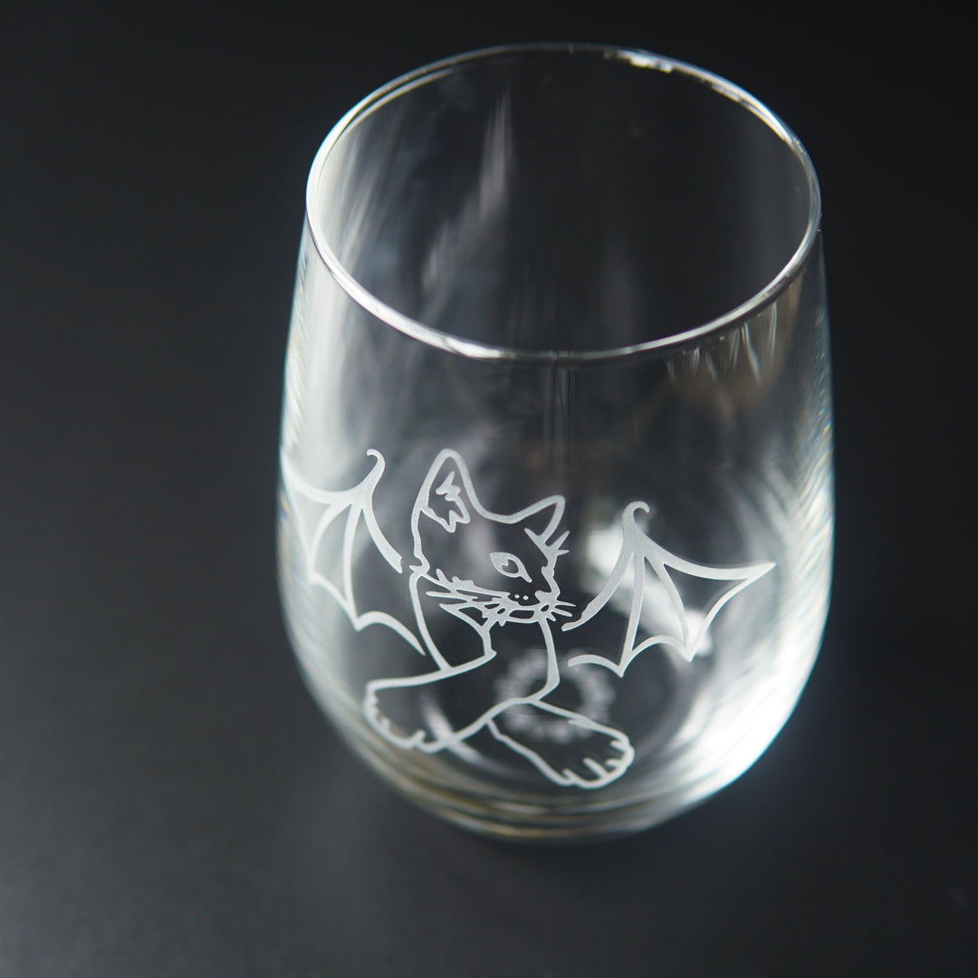 stemless wine glass engraved with a cat with crossed arms and bat wings. We're viewing the glass mostly from above