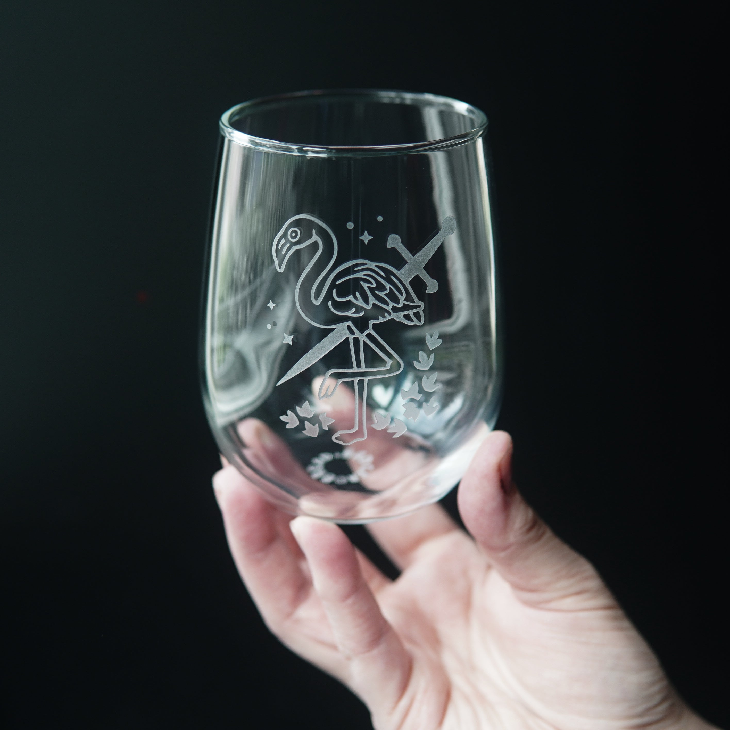 stemless wine glass etched with a flamingo and sword, held by a hand
