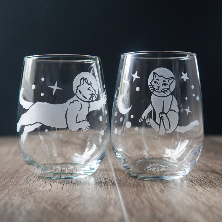 space cats engraved onto a pair of stemless wine glasses