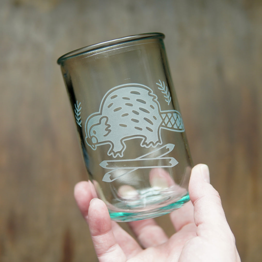 Beaver etched on a tall recycled glass cup, held in a hand
