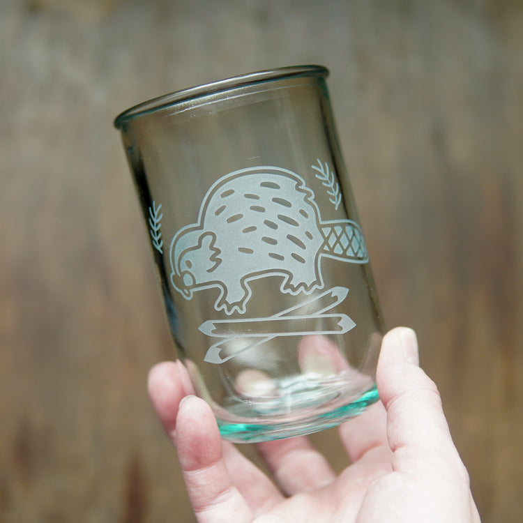 Beaver etched on a tall recycled glass cup, held in a hand