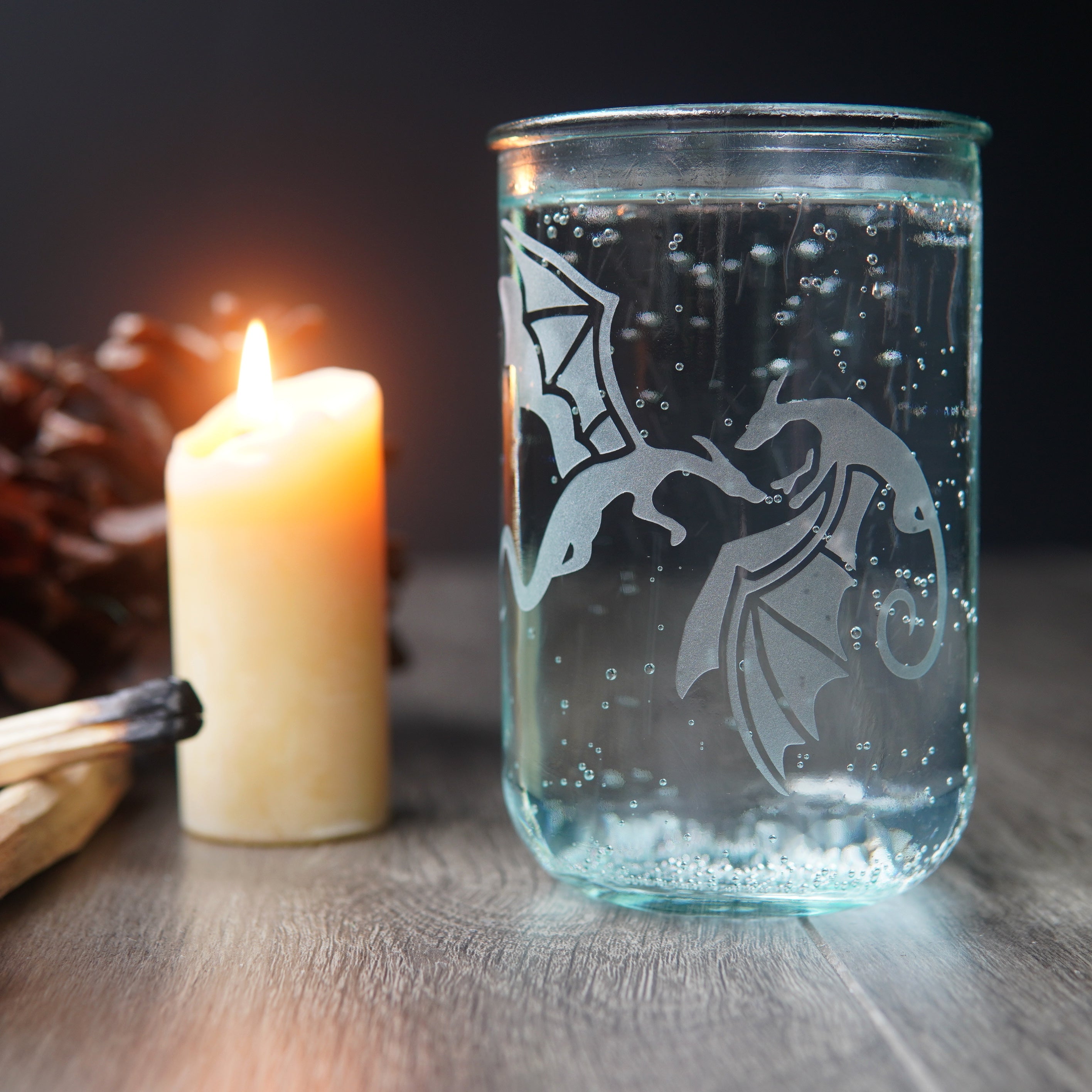 winged dragons etched on a tall glass full of seltzer, sitting next to a lit candle