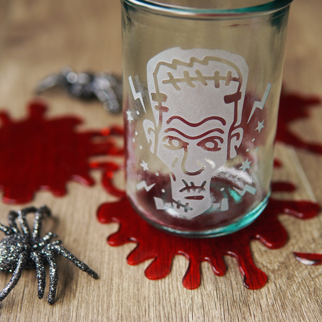 Frankenstein head etched onto a tall glass, sitting on fake blood spatters and spiders