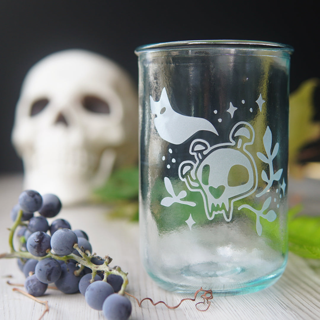haunted cat skull engraved drinking glass, next to a cluster of small grapes and a plastic skull