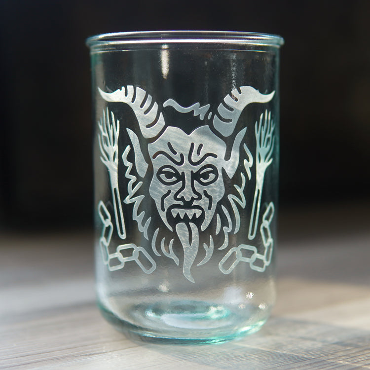 krampus with his tongue out, engraved on a bluegreen-tinted tall glass