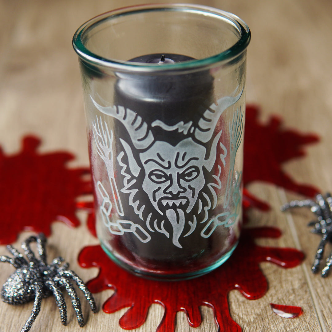 krampus engraved on a tall glass with black pillar candle, fake blood spatters, and glittery plastic spiders