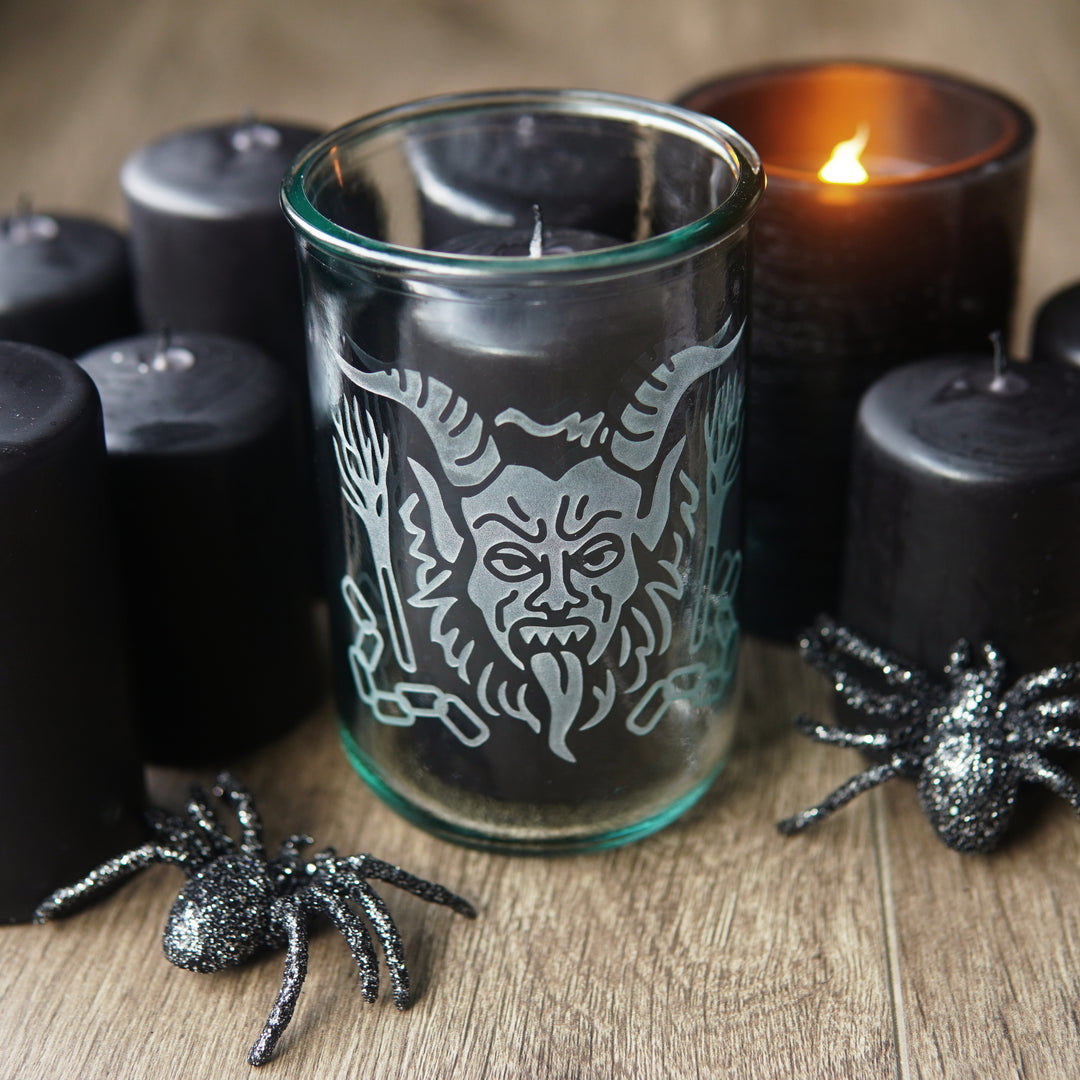 krampus engraved on a tall glass with black pillar candles and glittery plastic spiders
