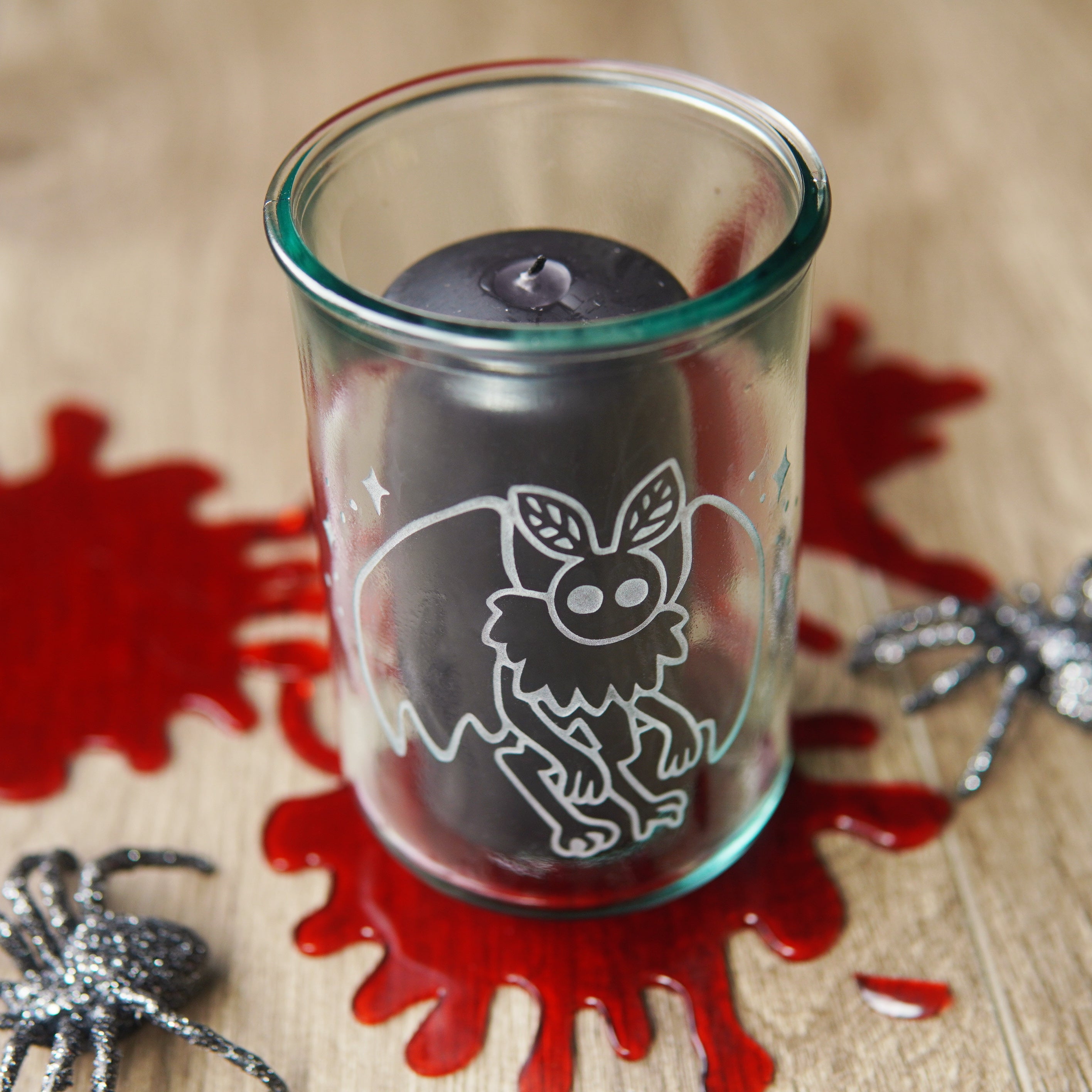 mothman etched onto a tall glass, with black pillar candle, fake blood splatters, and plastic spiders