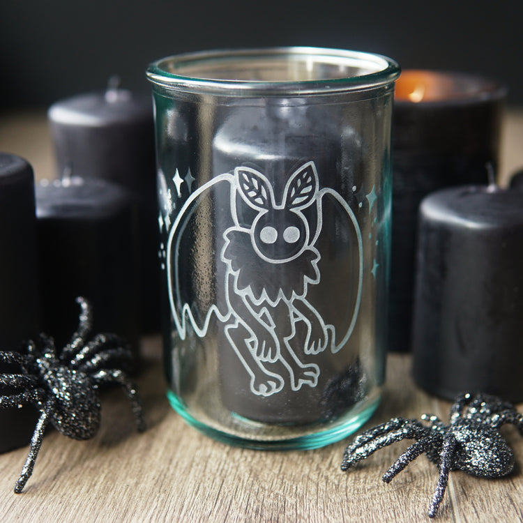mothman etched onto a tall glass, with black pillar candles and plastic spiders