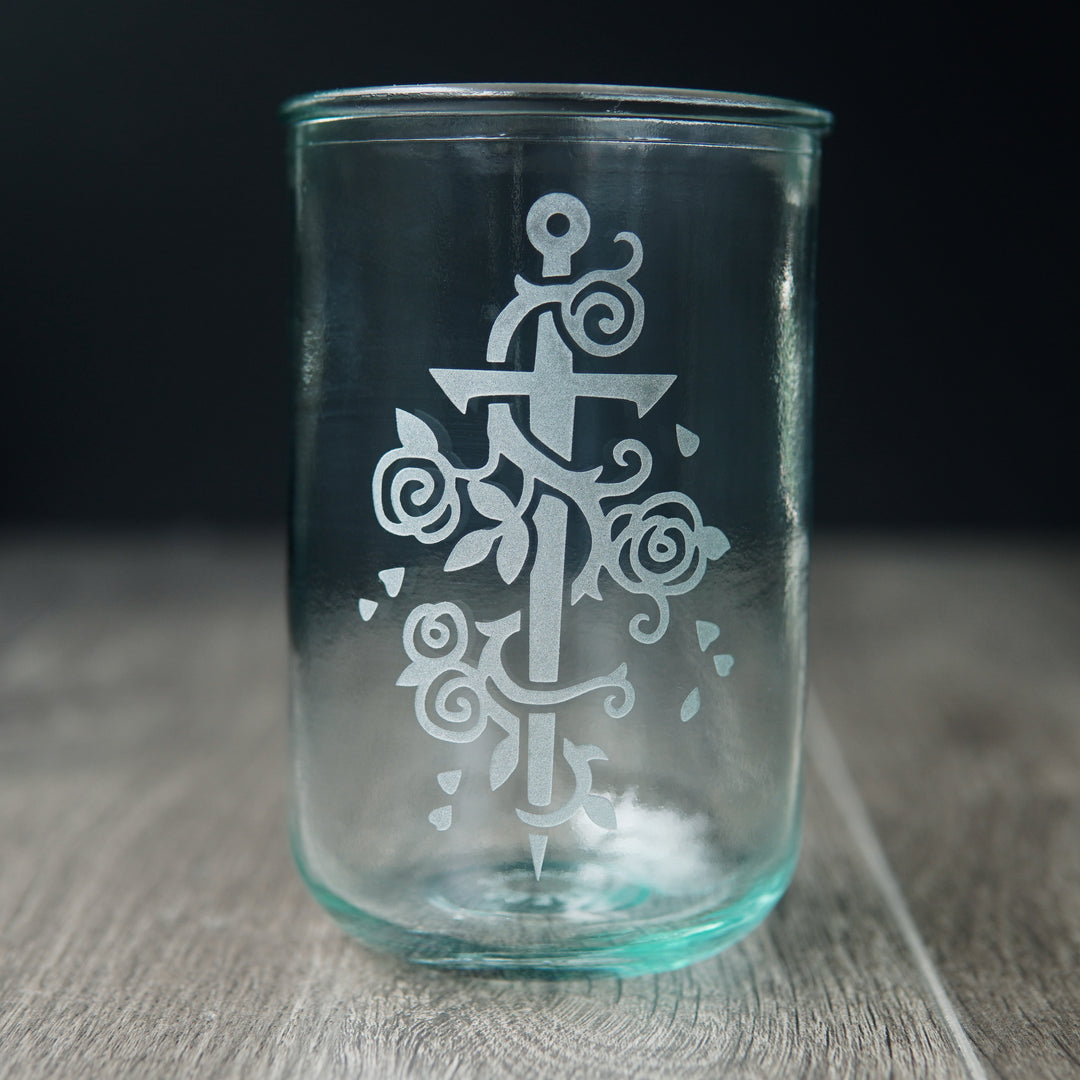 Sword wrapped with a rose vine engraved onto a tall drinking glass. The glass has a slight bluegreen tinge.