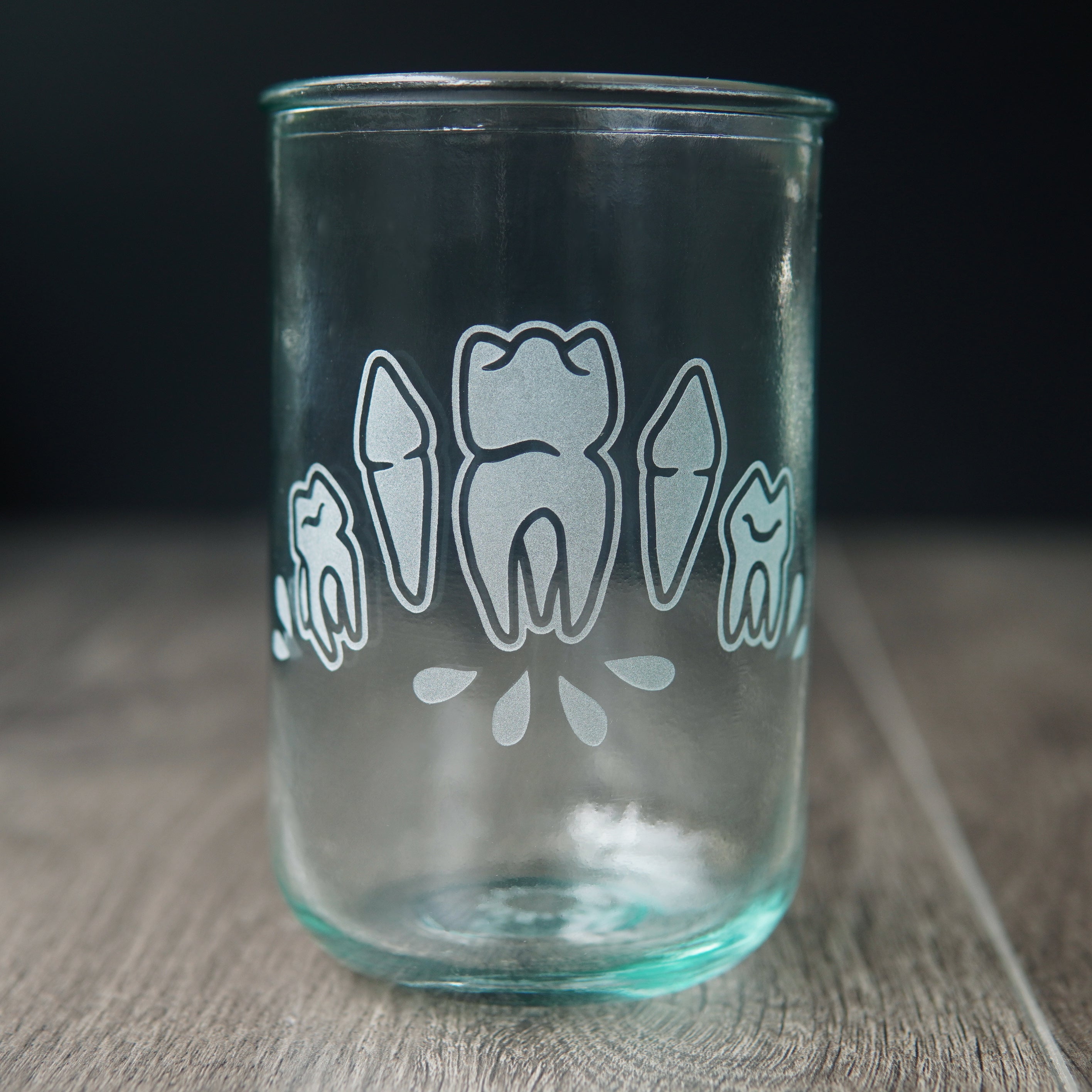 Four teeth with blood droplets engraved onto a tall drinking glass. The glass has a slight bluegreen tinge.