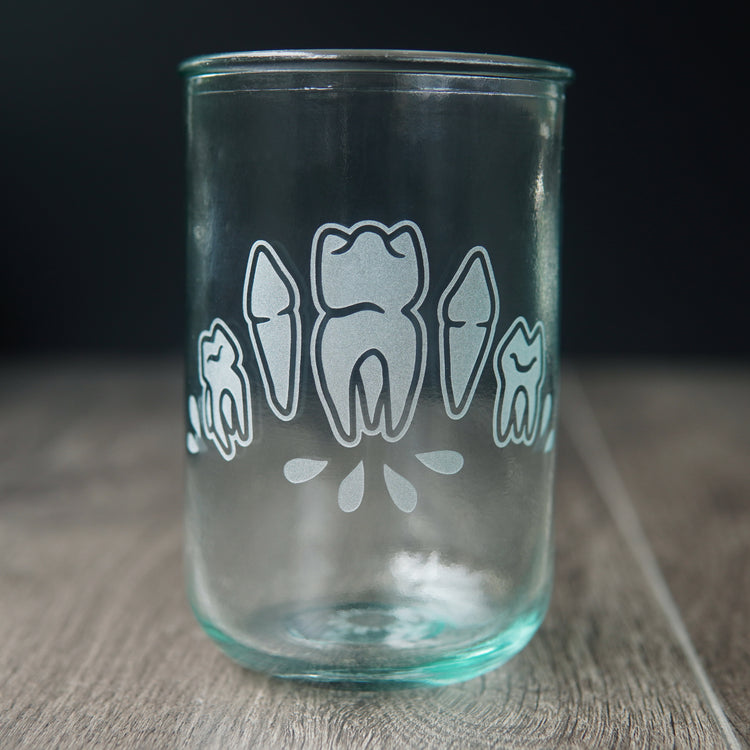 Four teeth with blood droplets engraved onto a tall drinking glass. The glass has a slight bluegreen tinge.