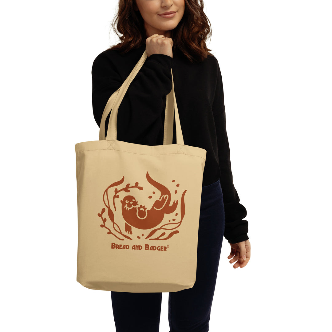 Woman holding a beige tote bag with a brown otter and 'Bread and Badger' text on a white background