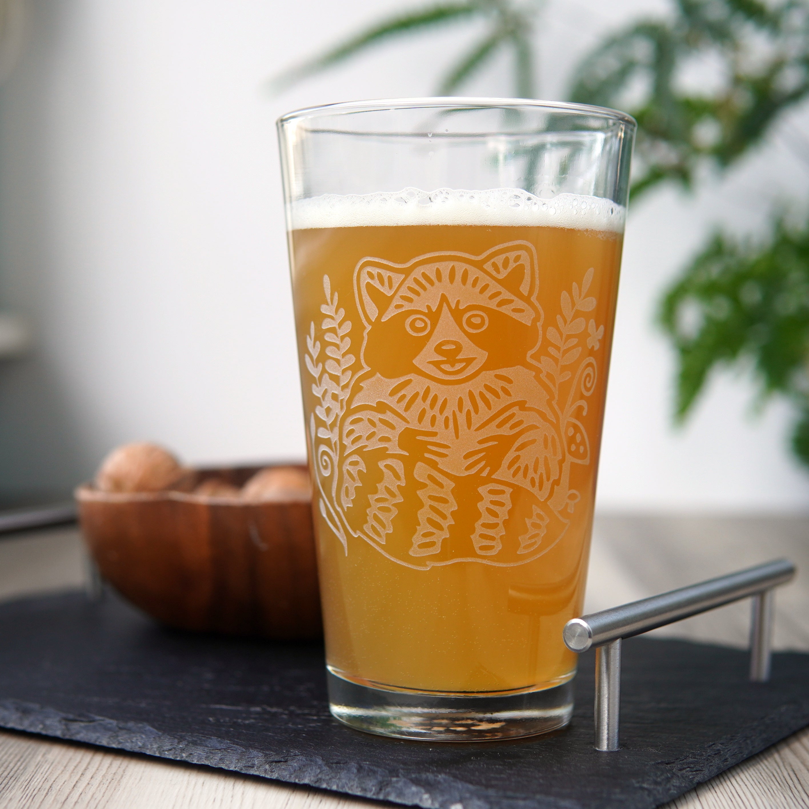etched pint glass engraved with a cute, smiling raccoon, full of hazy beer