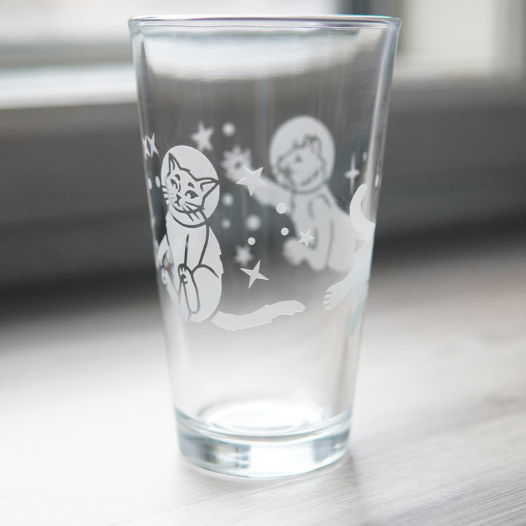 a pint glass engraved with space cats all over it