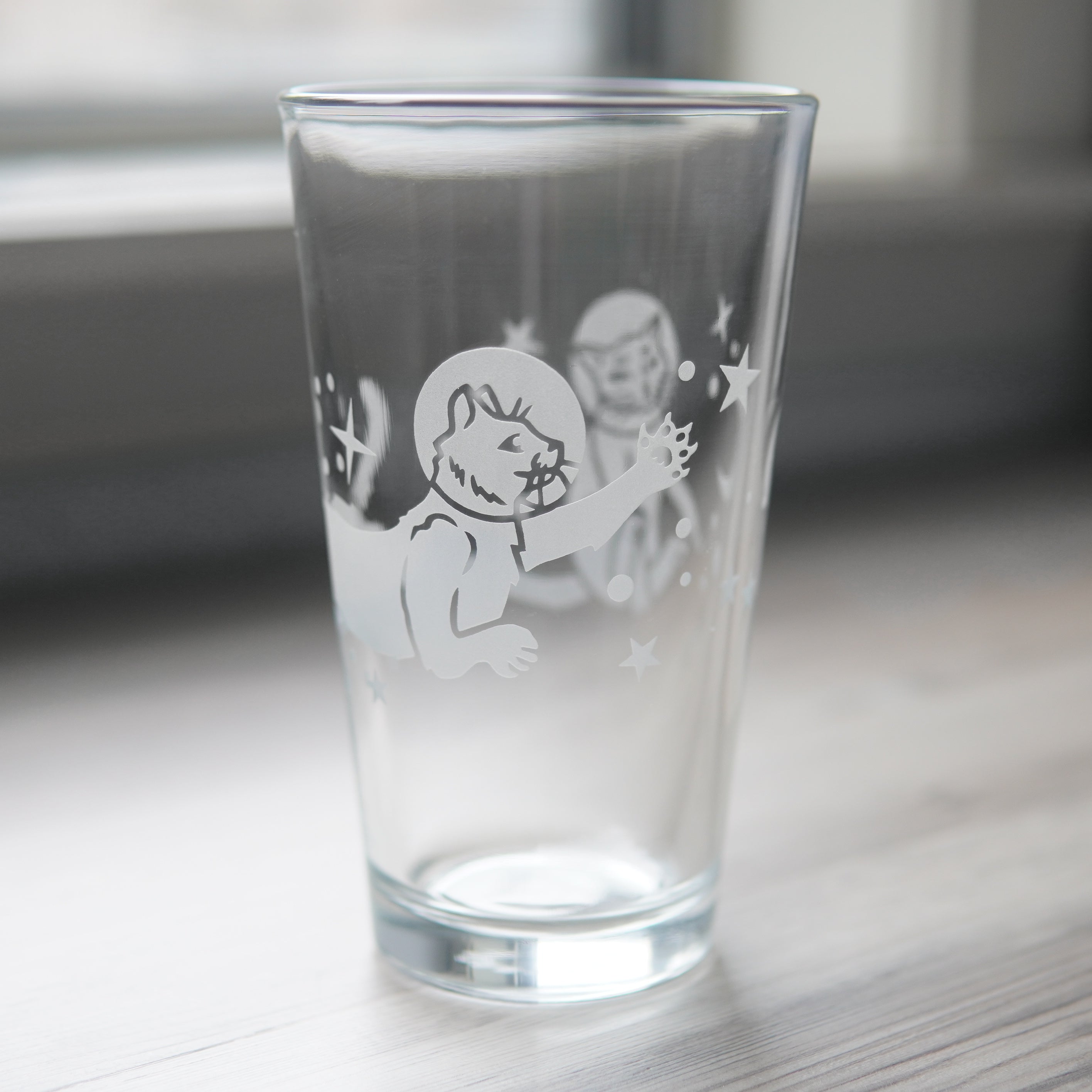 a pint glass engraved with space cats all over it