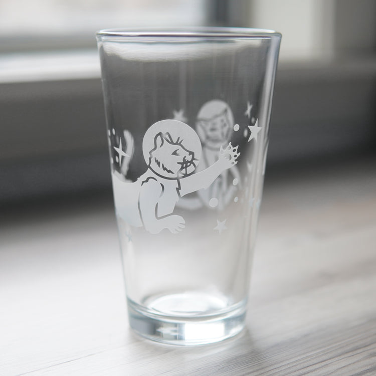 a pint glass engraved with space cats all over it