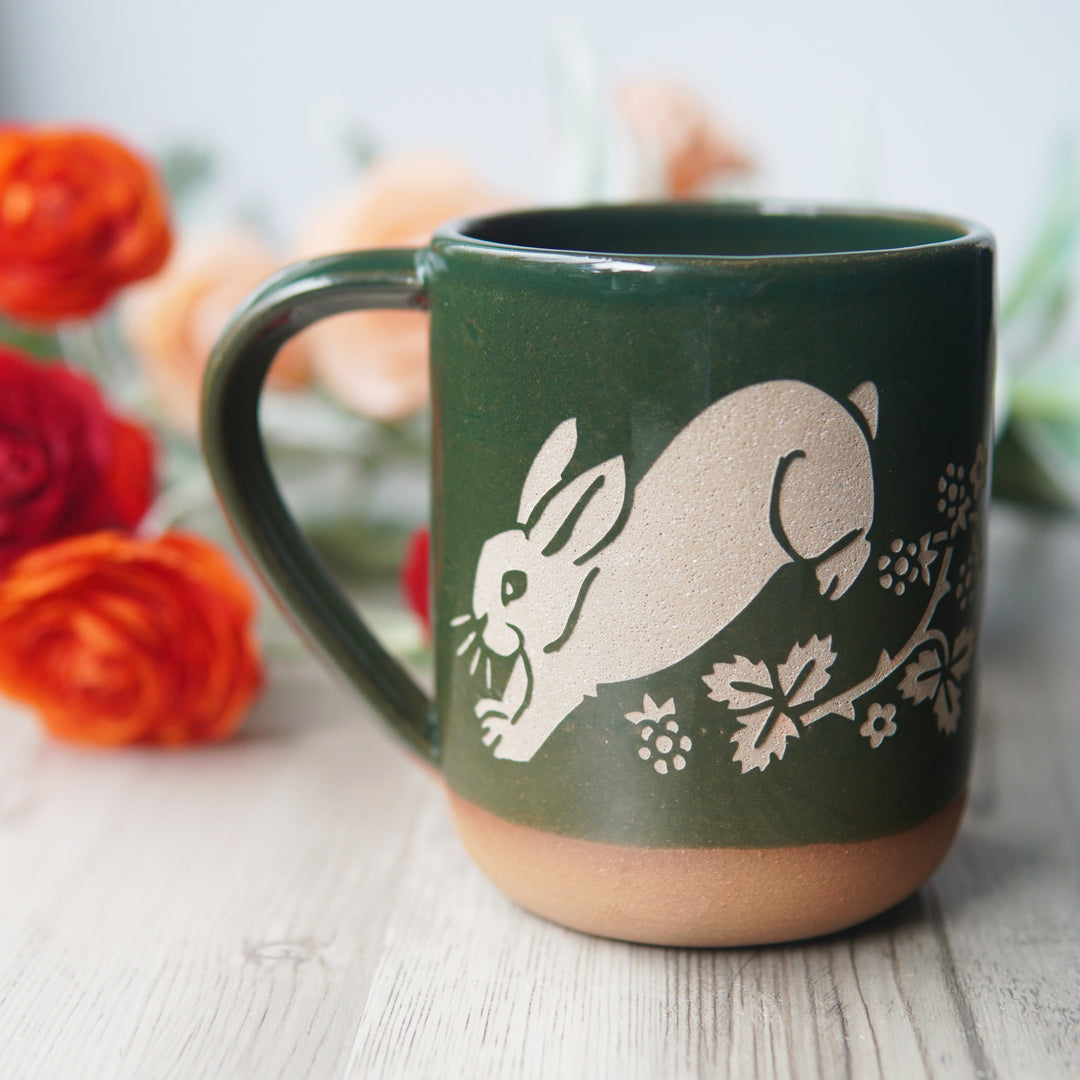 pine green rabbit mug in front of red and orange ranunculus flowers