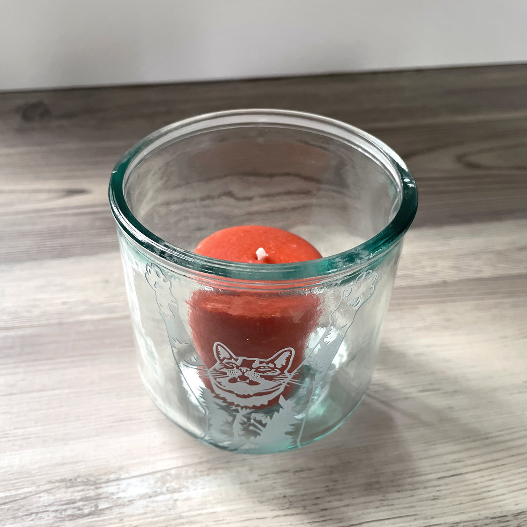 top half of a tabby cat with its arms stretched up and mouth slightly open engraved onto a short glass holding a votive candle