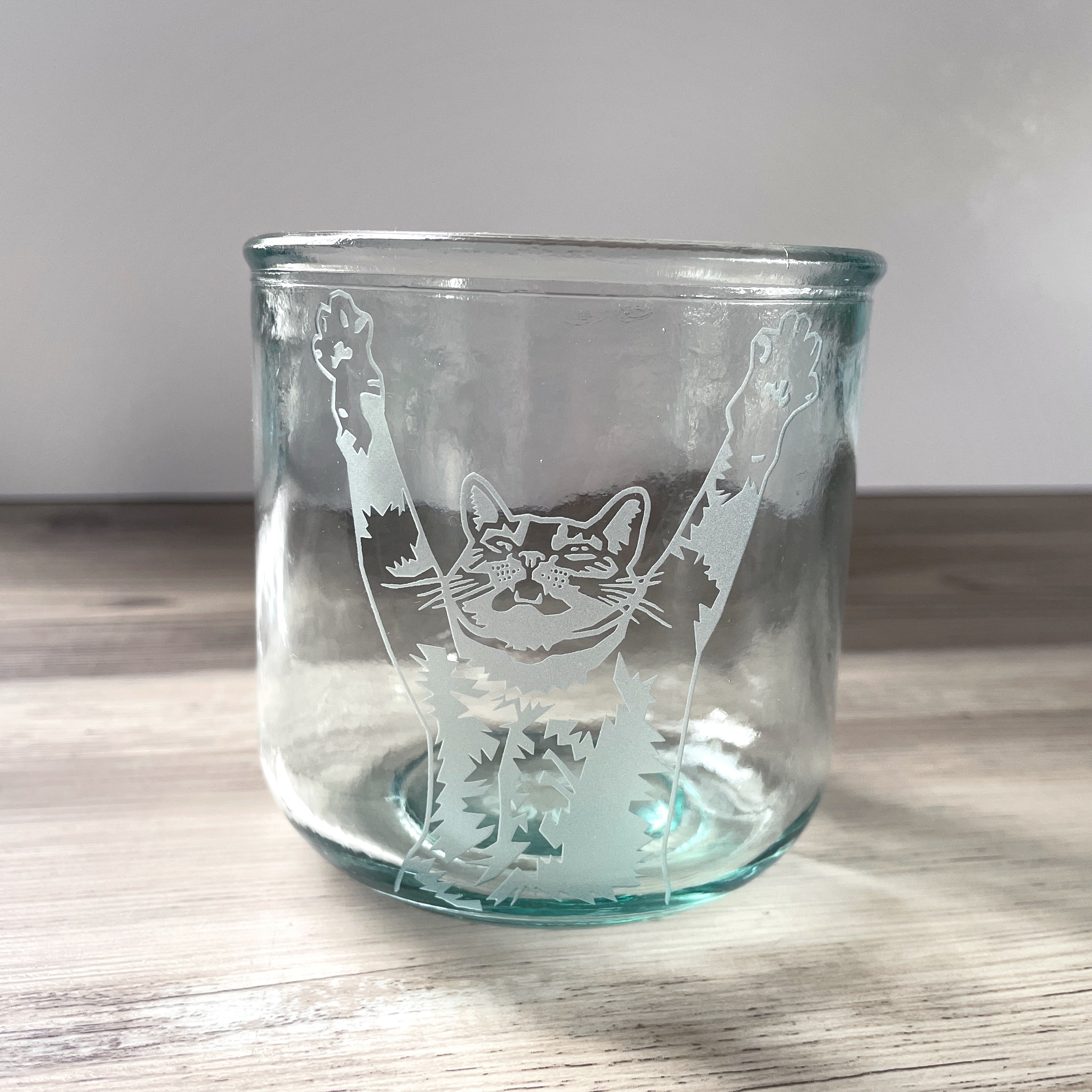 top half of a tabby cat with its arms stretched up and mouth slightly open engraved onto a short glass