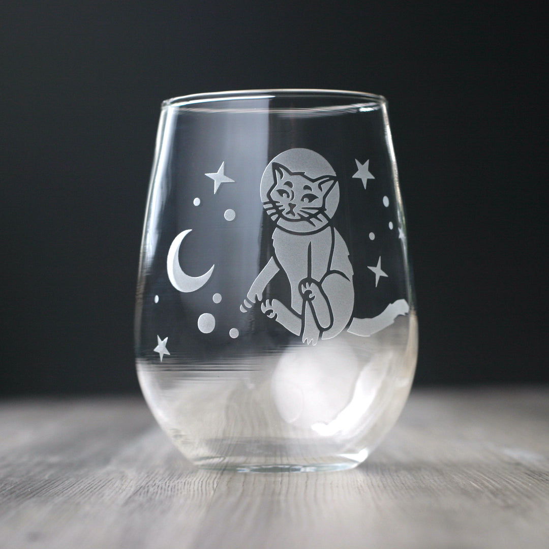 an astronaut cat floating in the stars near a crescent moon, engraved onto a stemless wine glass.