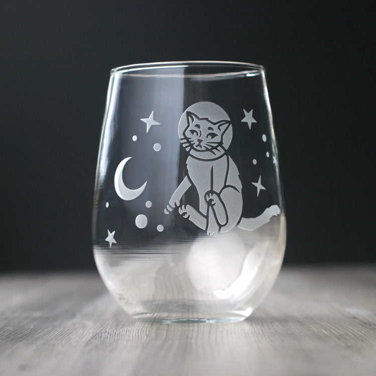 an astronaut cat floating in the stars near a crescent moon, engraved onto a stemless wine glass.