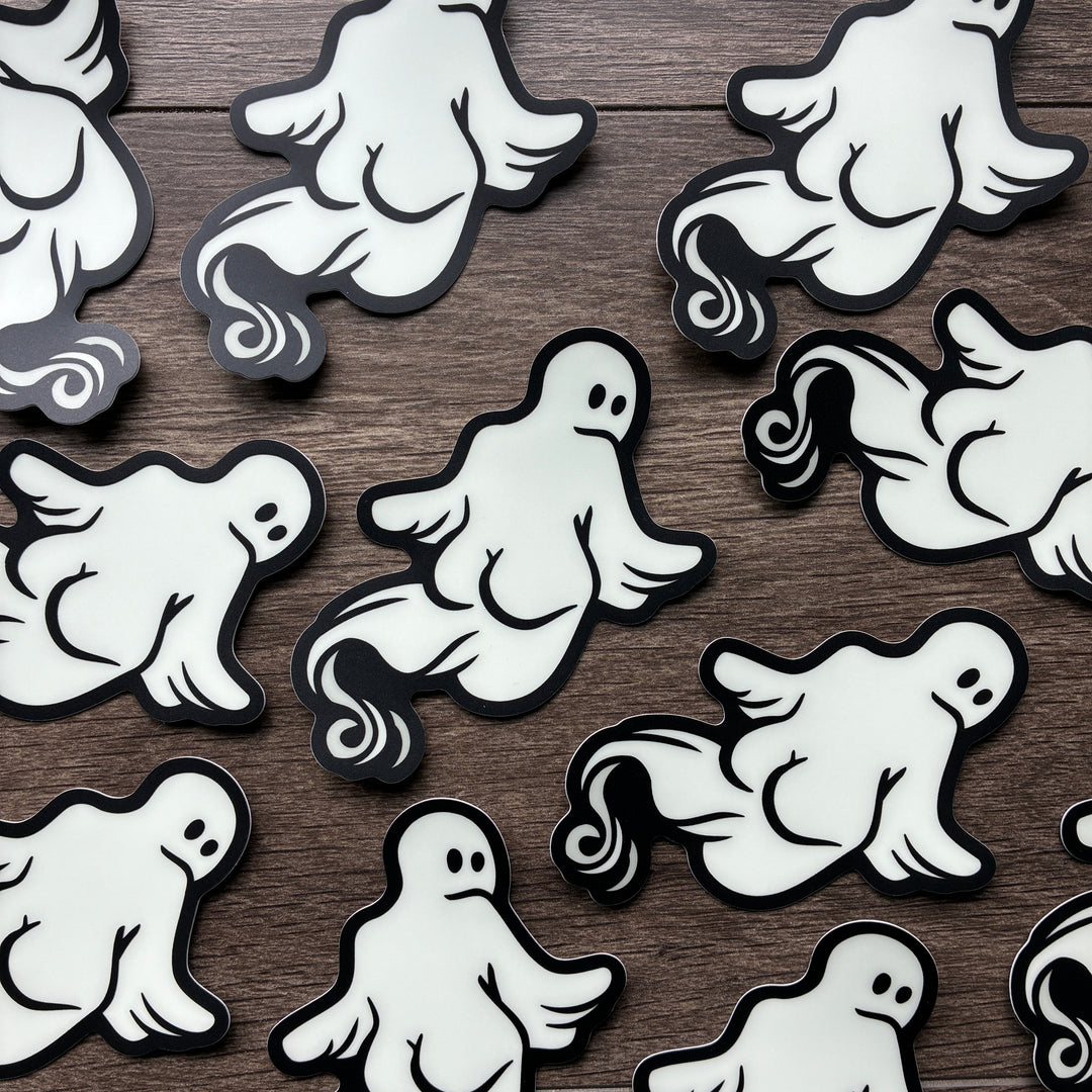 White ghost-shaped stickers with black outlines scattered on a dark brown wood background.