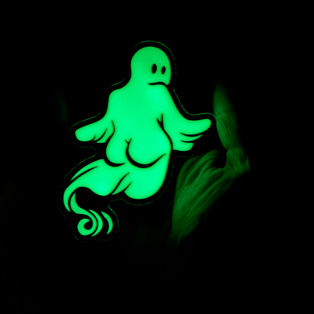 A glowing green cartoon ghost-shaped item on a black background, with a faint hand visible at the right edge.
