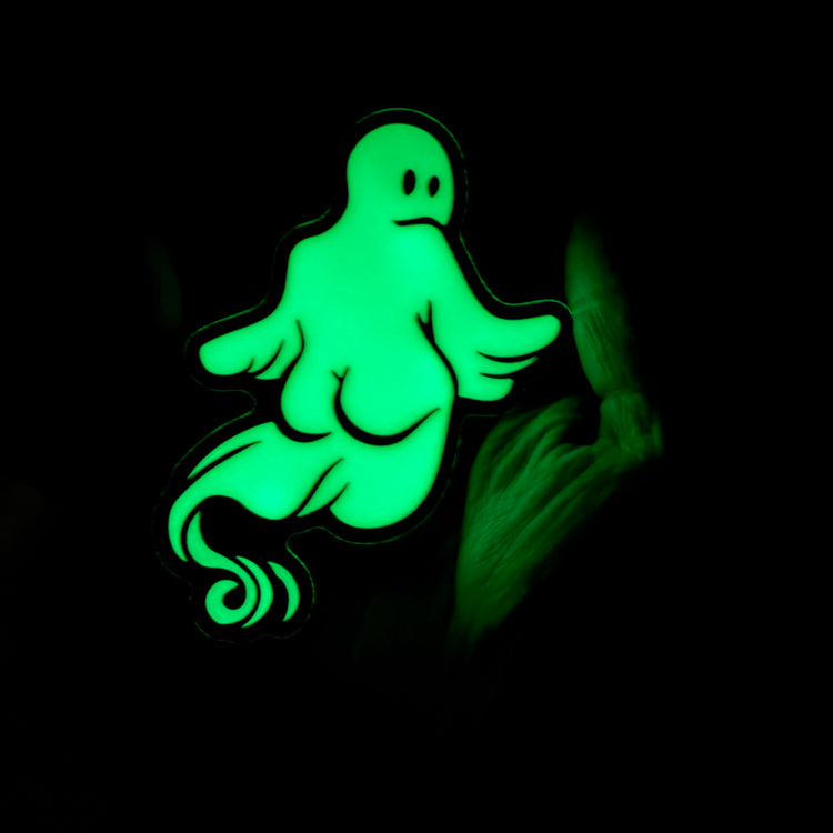 A glowing green cartoon ghost-shaped item on a black background, with a faint hand visible at the right edge.
