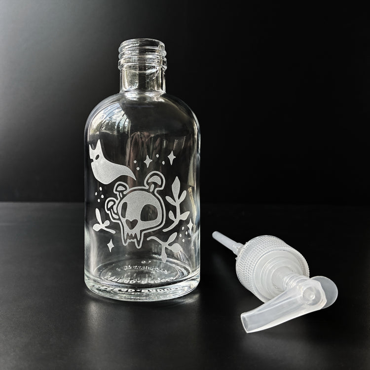 Clear glass bottle with decorative etching of a ghost and cat skull on a black background