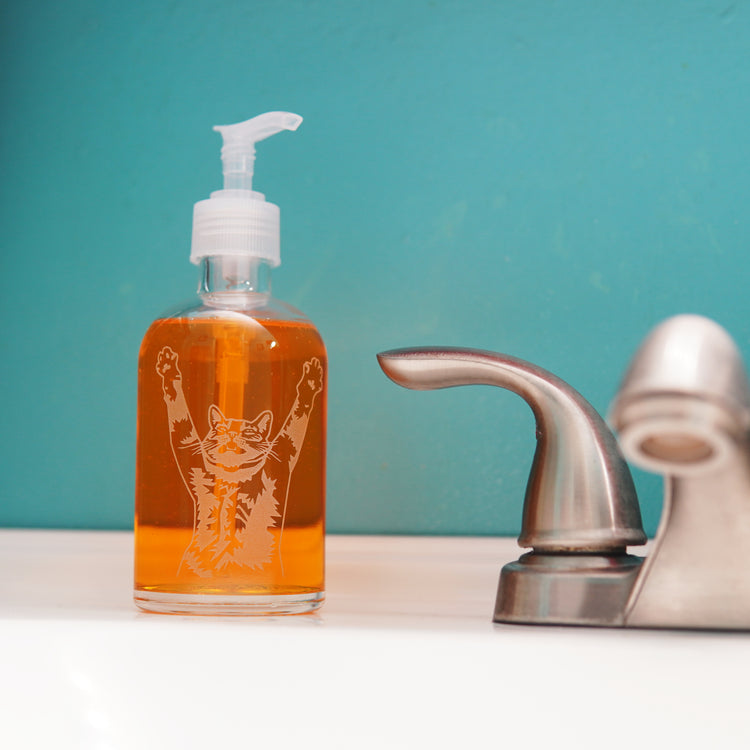 cat soap dispenser; apothecary pump bottle next to a bathroom sink faucter