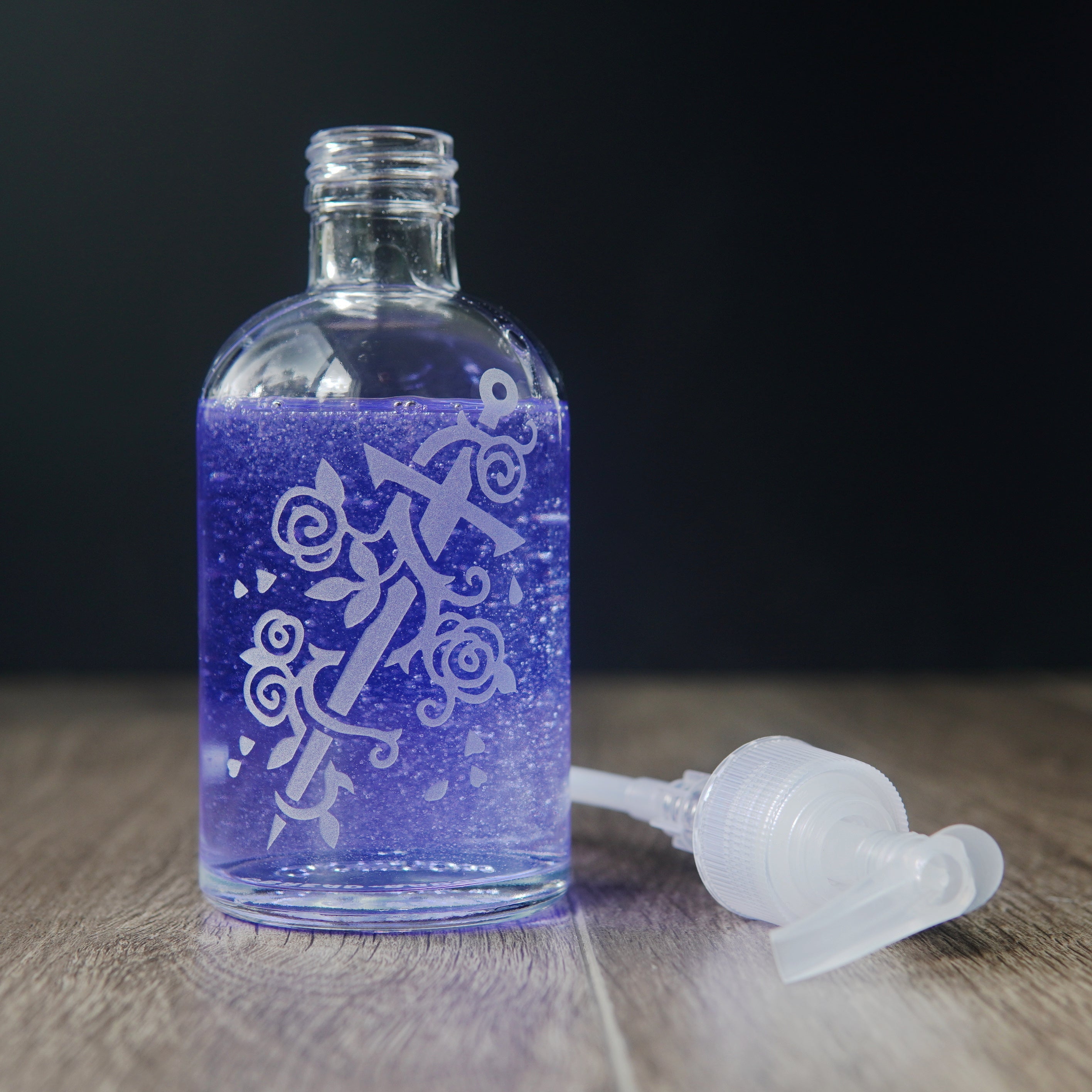 glass soap dispenser engraved with a sword wrapped with a rose vine. the pump bottle is filled with light purple liquid soap