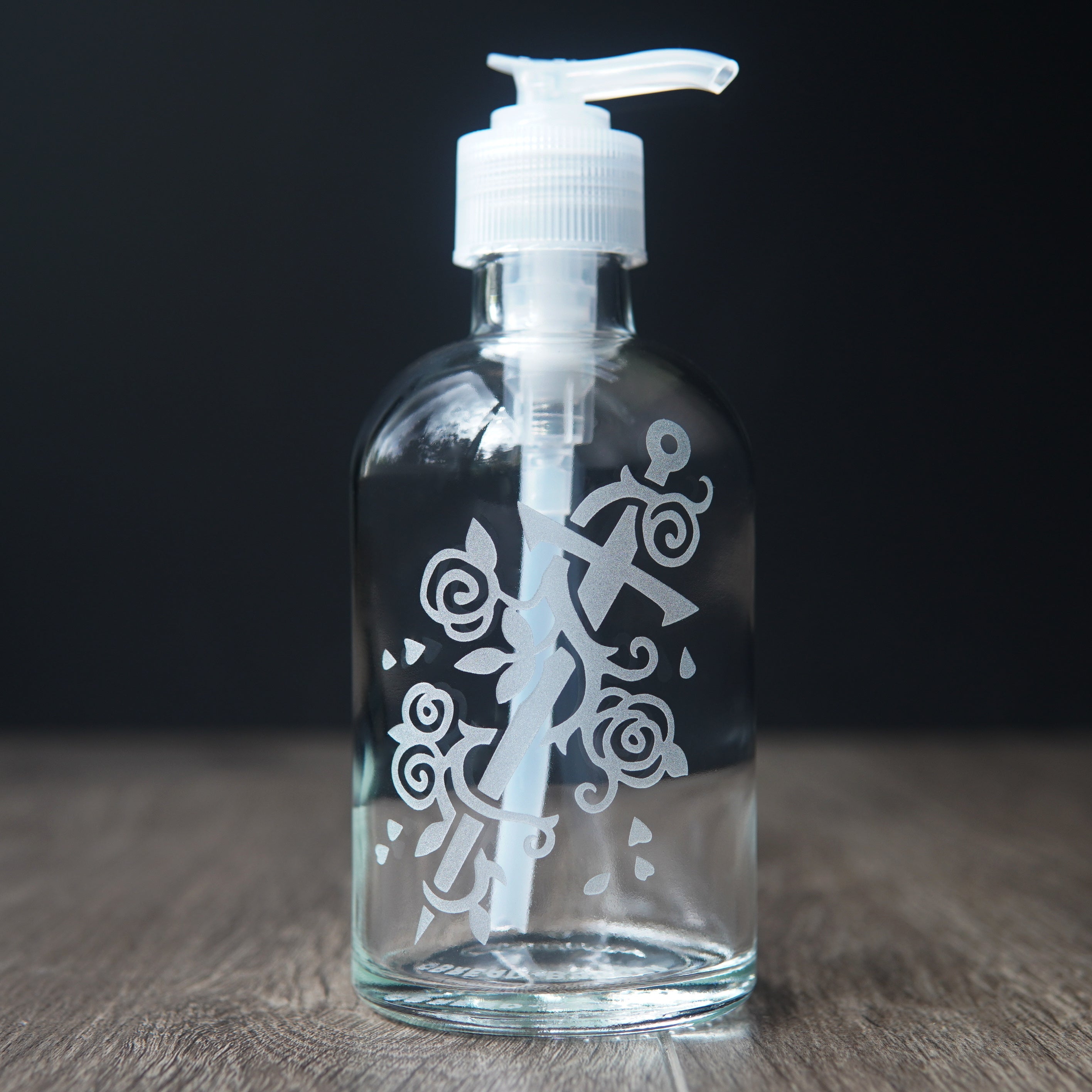 glass soap dispenser engraved with a sword wrapped with a rose vine.