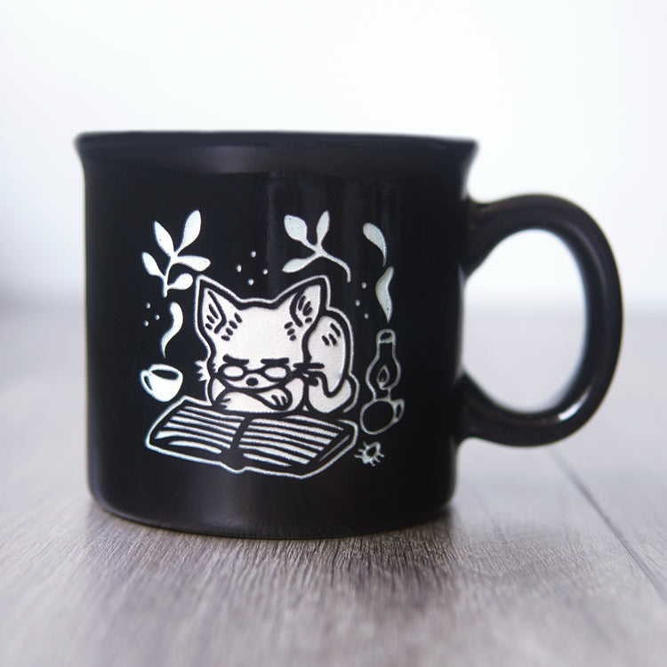Black mug with a white cat illustration on a wooden surface