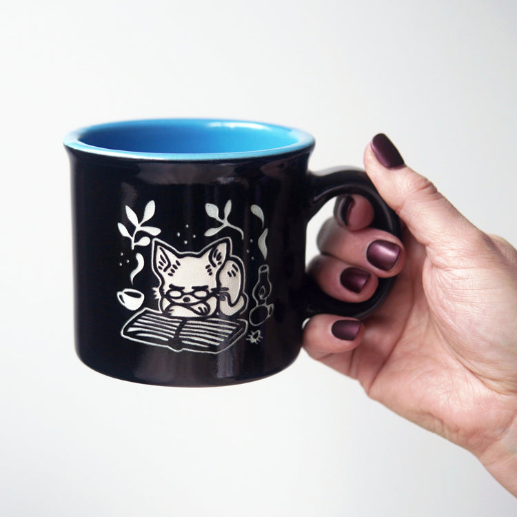 Black mug with a cat design held by a hand against a white background