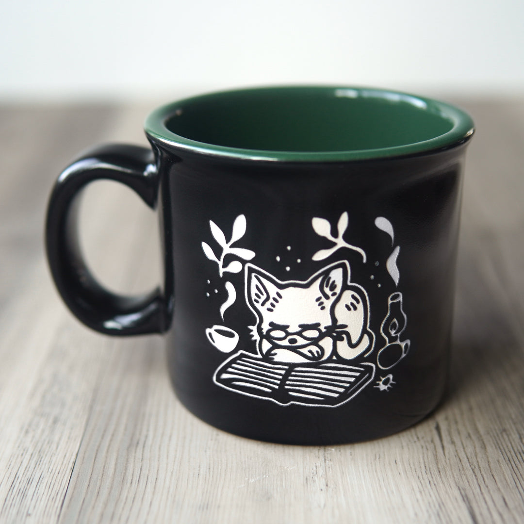 Black mug with a white cat illustration and green interior on a wooden surface