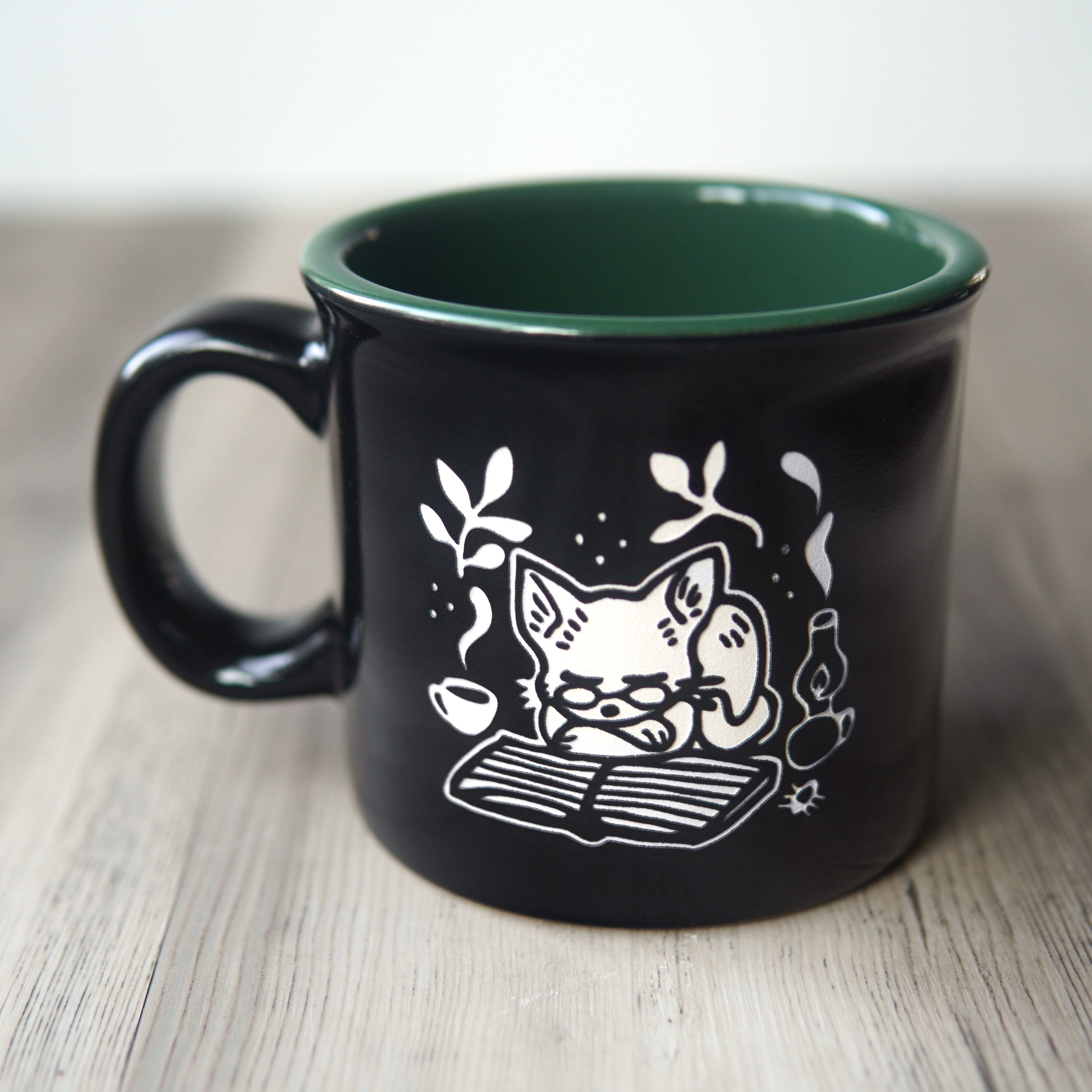 Black mug with a white cat illustration and green interior on a wooden surface