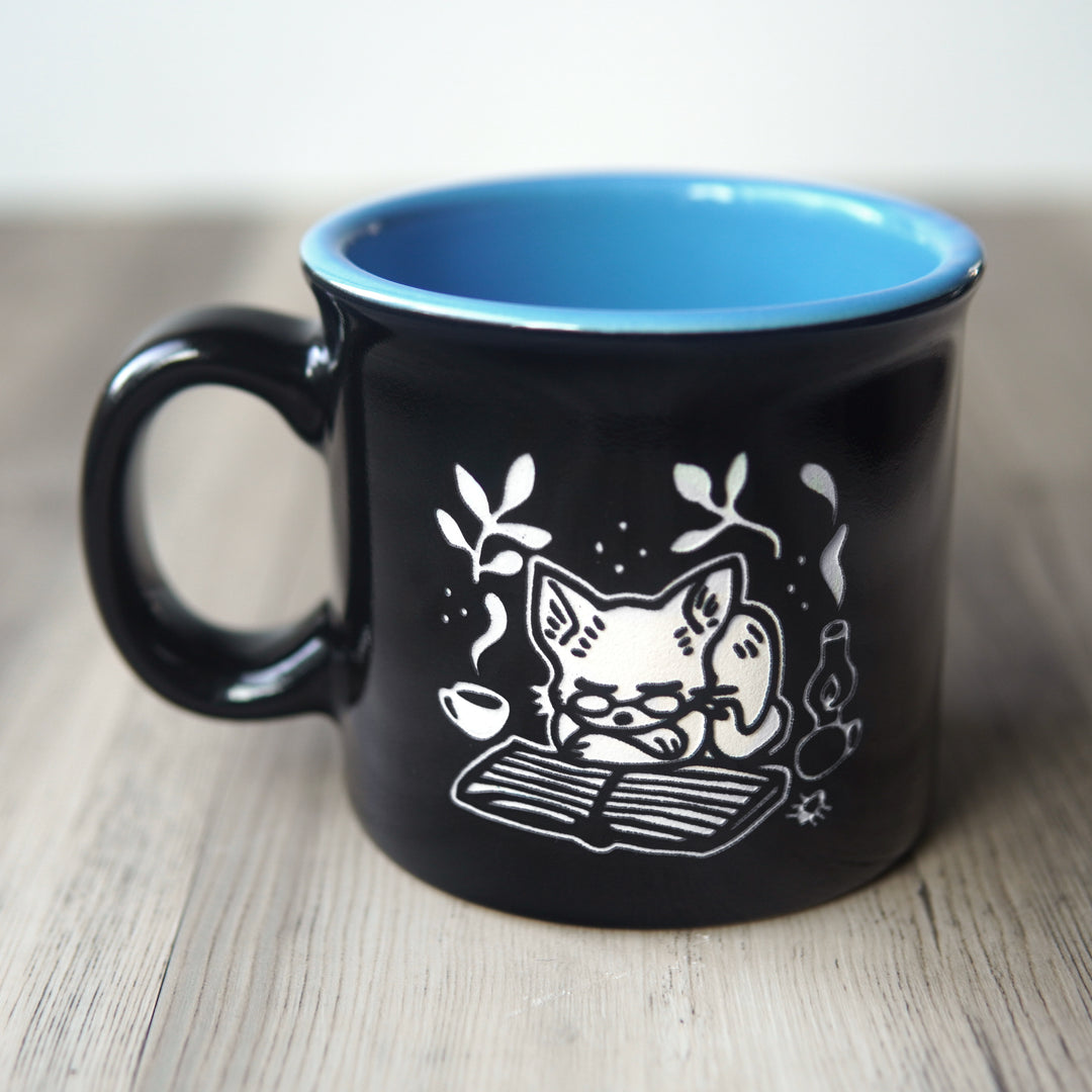 Black mug with a white cat illustration and blue interior on a wooden surface