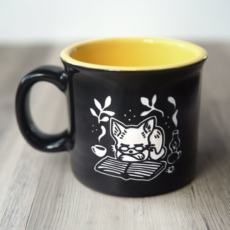 Black mug with a white cat illustration and yellow interior on a wooden surface