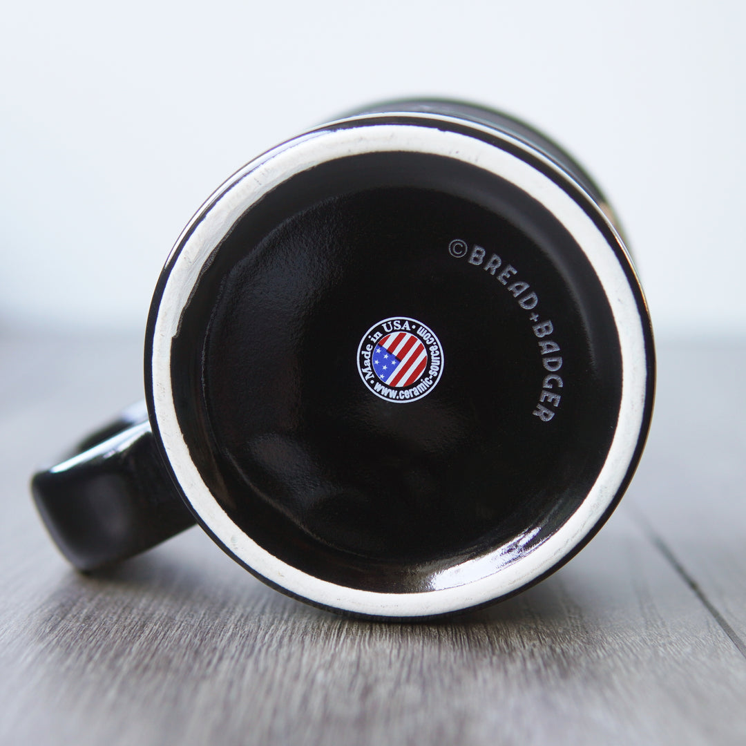Bottom of a black mug with "Made in USA" decal and "(C) Bread + Badger" sitting on a light wooden surface.