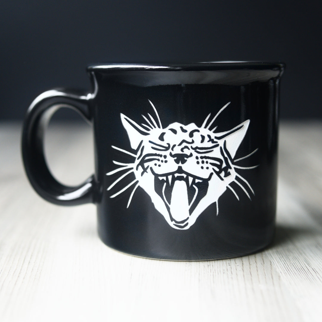 Black mug with a white cat design on a wooden surface