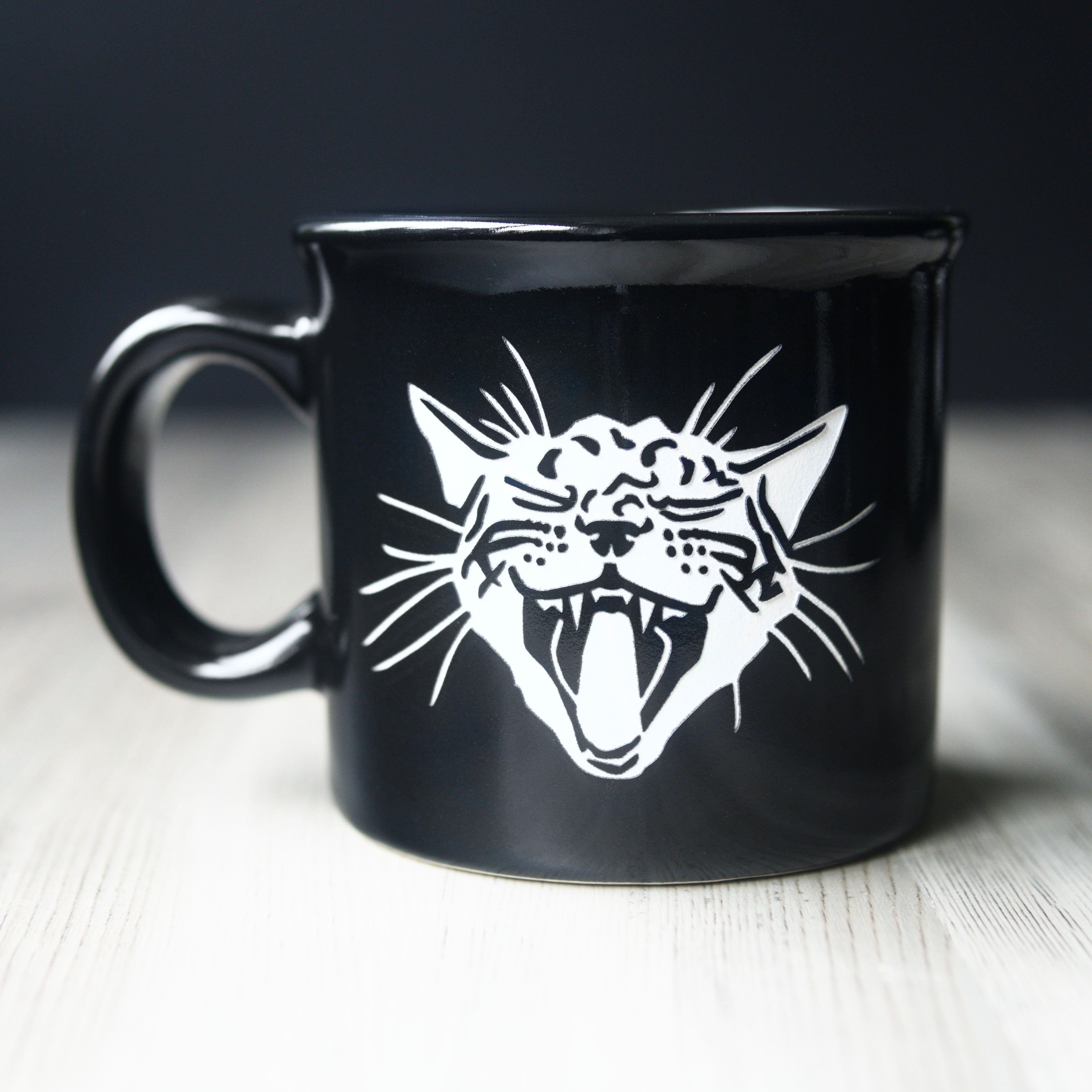 Black mug with a white cat design on a wooden surface
