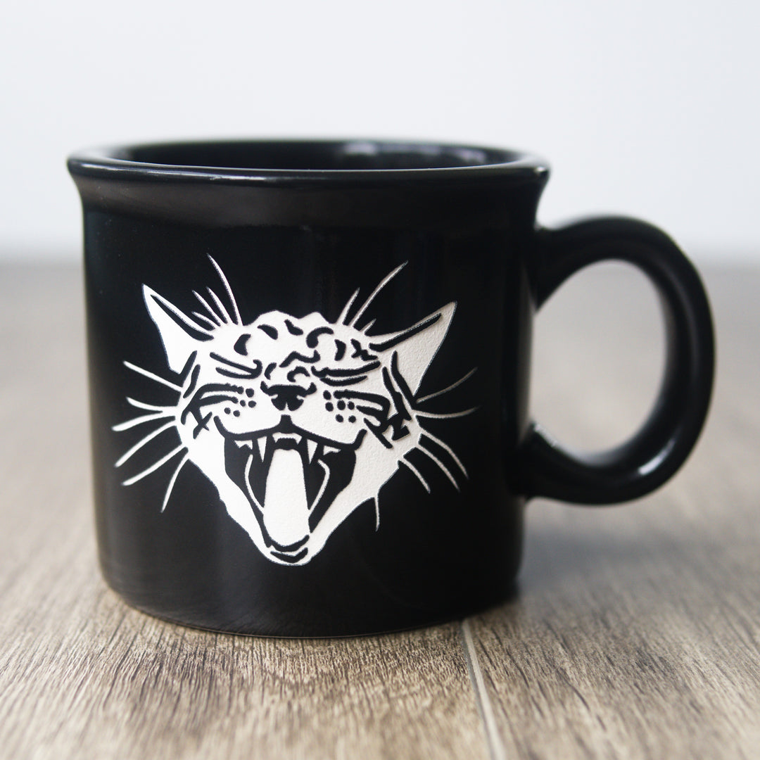 Black mug with a white cat illustration on a wooden surface
