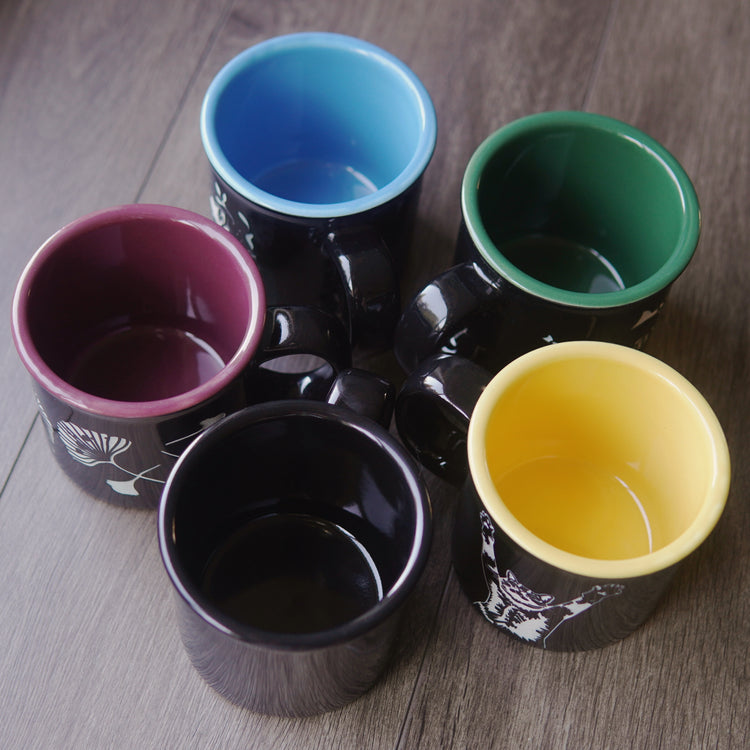 Five black mugs with colored interior on a wooden surface
