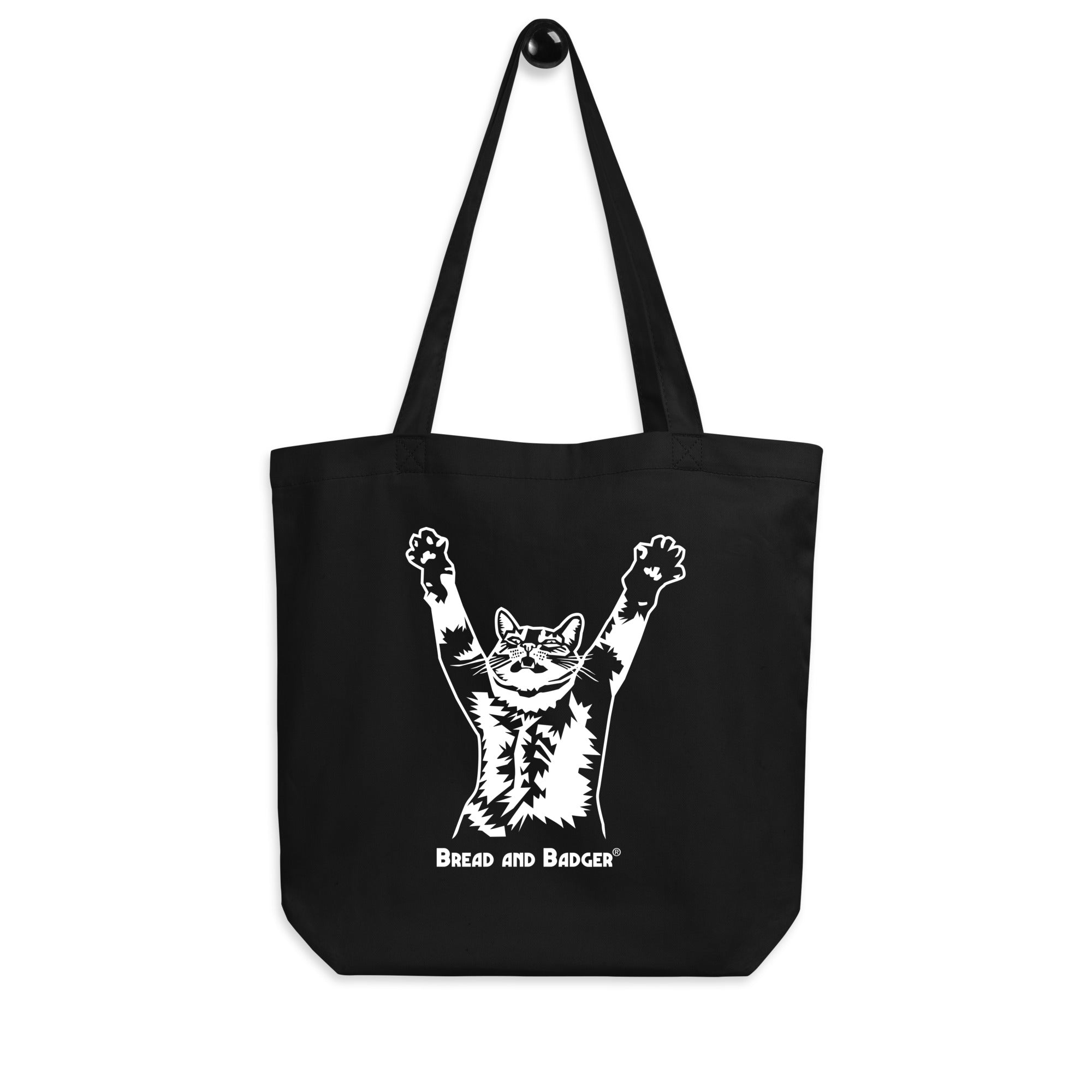 A black organic cotton tote bag featuring a white graphic of a stretching cat on the front.