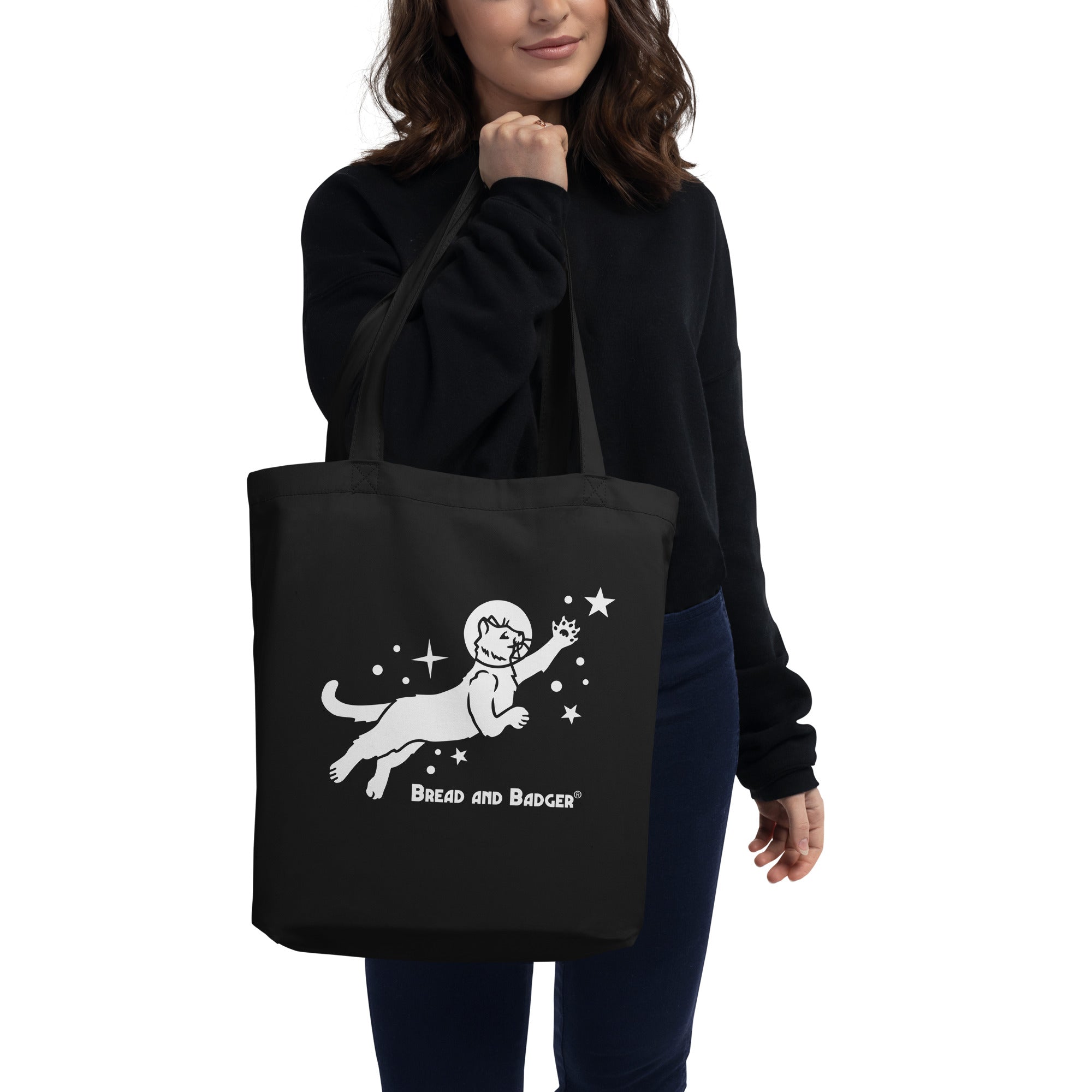 Woman holding a black tote bag with white astronaut cat graphic and 'Bread and Badger' text on a white background